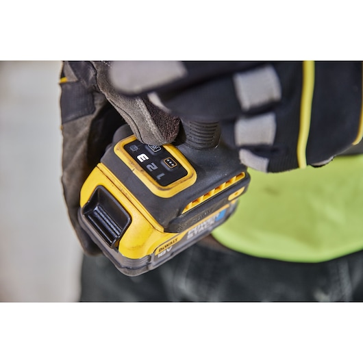 Gloved hand adjusts settings on a yellow DEWALT power tool, focusing on control buttons and display panel.