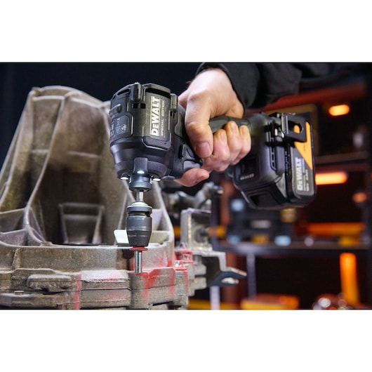 Hand uses DEWALT impact driver DCF86MM2T to fasten bolt in metal part within workshop setting.