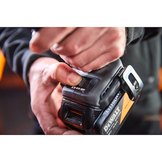 Close-up of a hand operating a DEWALT lithium battery tool, showing the battery and tool details.