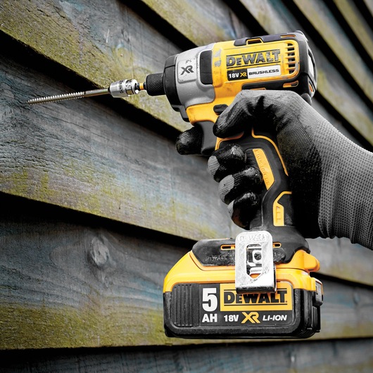 DEWALT DCF887P2 18V XR impact driver drilling into wooden planks, held by gloved hand.