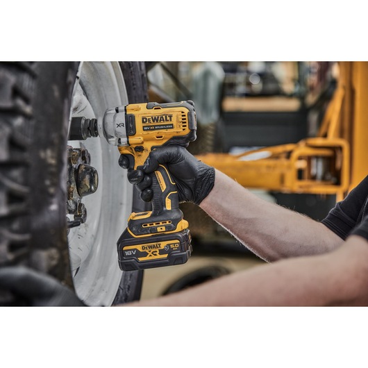A person wearing black gloves uses a DEWALT DCF891NT 18V XR brushless impact wrench to work on the wheel of a vehicle.