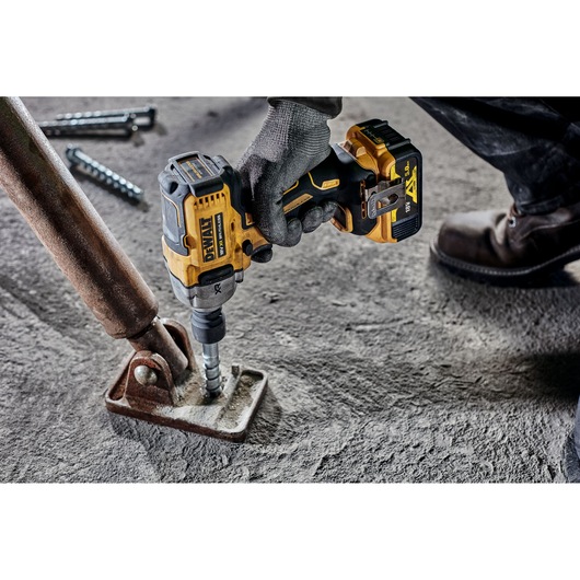 A gloved hand operating a DEWALT cordless impact wrench (DCF891NT) to fasten a metal base to a concrete floor.