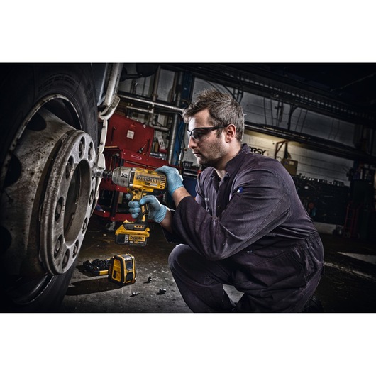 A person wearing work gloves and coveralls is using a yellow DEWALT impact wrench to loosen the bolts on a large vehicle