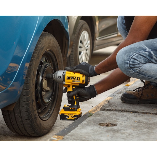 A person wearing gloves uses a DEWALT cordless impact wrench to loosen or tighten lug nuts on a car wheel.