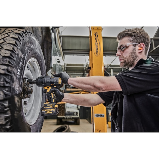 A person using a DEWALT DCF900P2G cordless impact wrench to tighten or loosen the bolts on a vehicle wheel inside a garage