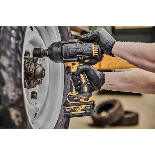 A person wearing black gloves is using a DEWALT DCF900P2G cordless impact wrench to loosen or tighten bolts on a vehicle