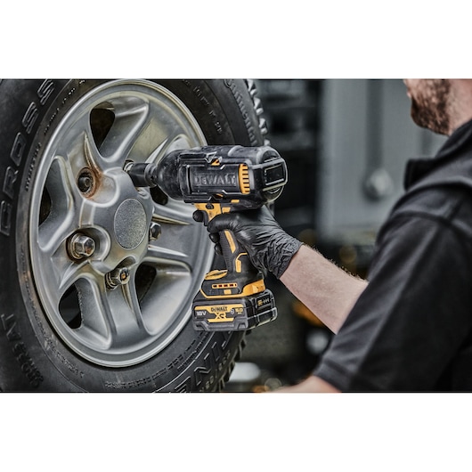 A person is using a DEWALT cordless impact wrench to remove or tighten a lug nut on a car wheel. The tool is held with a