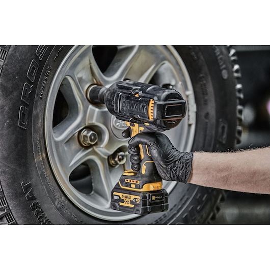 A person wearing a black glove uses a DEWALT cordless impact wrench to tighten or loosen lug nuts on a car wheel.