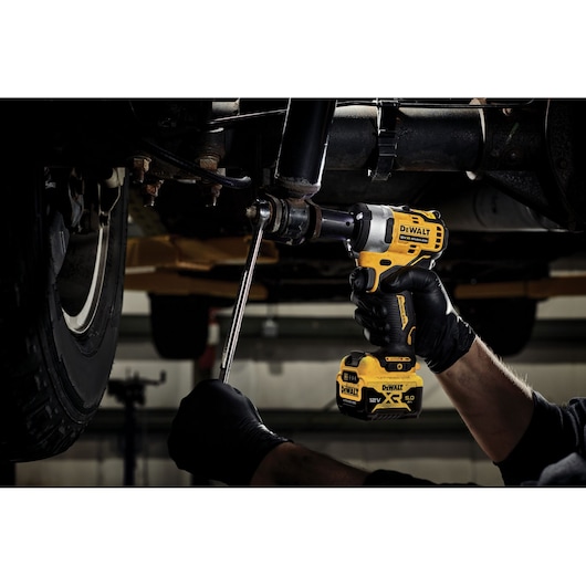 A person wearing black gloves uses a DEWALT 12V cordless impact wrench to work on the underside of a vehicle.