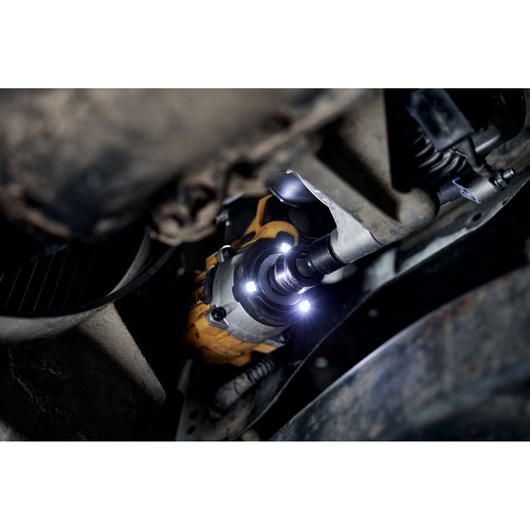 DEWALT power tool with LED lights in use on a vehicle part in a dimly lit area.