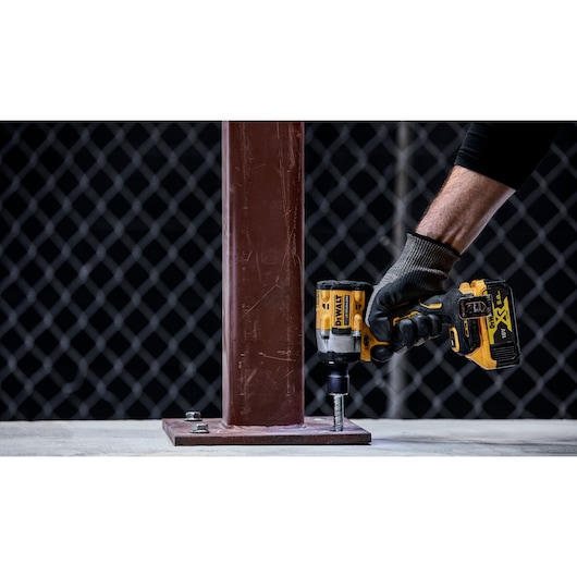 A person wearing a work glove uses a DEWALT DCF921NT cordless impact wrench to tighten a bolt at the base of a metal column.