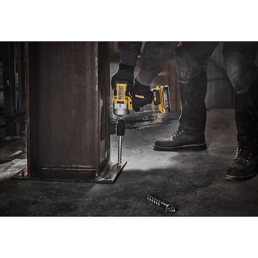 A person uses a DEWALT cordless impact wrench (model DCF961H2T) to tighten a large bolt at the base of a metal beam on an