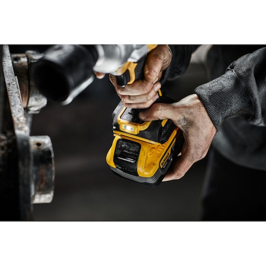Person using a DEWALT cordless power tool with yellow battery in an industrial setting.