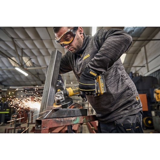 DEWALT angle grinder cutting metal with sparks. Worker wearing gloves in an industrial workshop.