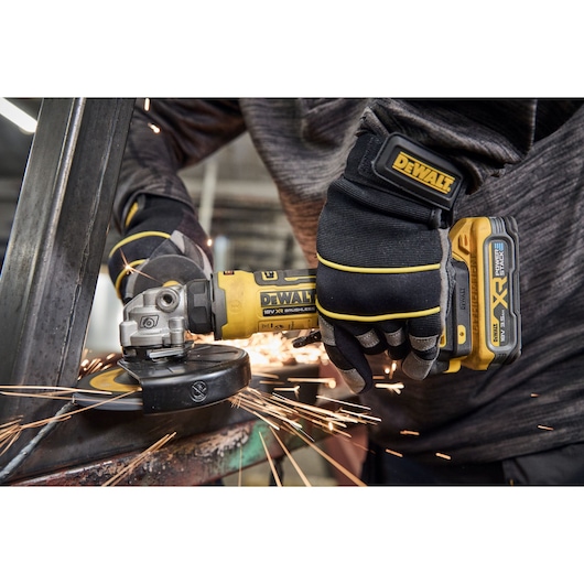 Person using a DEWALT cordless angle grinder on metal, sparks flying during operation.