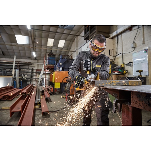 Worker uses DEWALT DCG404S2T-QW, DCG404S2T tool to grind metal in workshop, sparks flying.