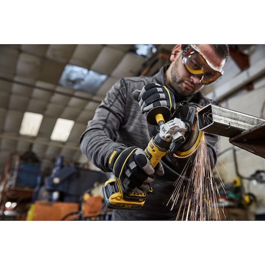 DEWALT DCG404S2T-QW, DCG404S2T used for grinding metal in workshop, sparks flying, person’s face blurred.