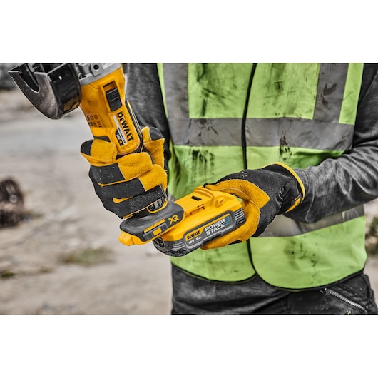 Person in work gloves holding a DEWALT cordless power tool with POWERSTACK battery outdoors.
