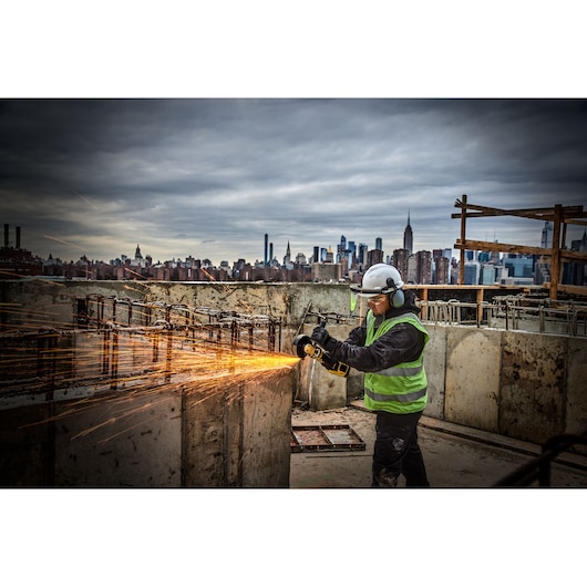 Person using a DEWALT cordless angle grinder on a concrete block, producing dust indoors.