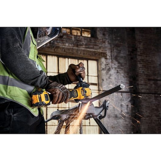 Worker uses a DEWALT angle grinder to cut metal rebar, sparks flying, in an industrial setting.