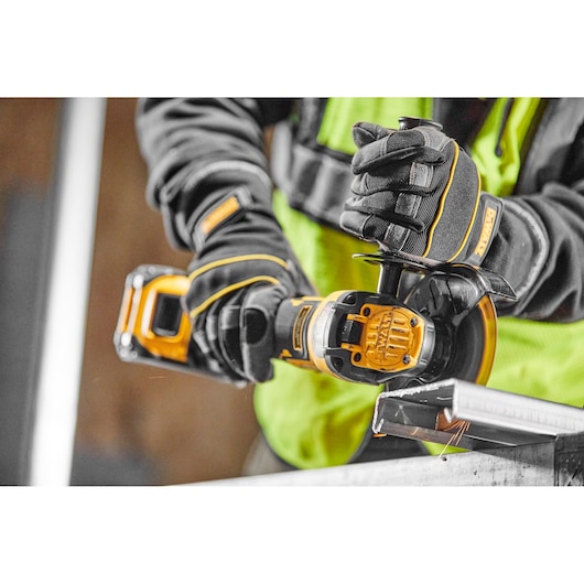 Person using a DEWALT cordless angle grinder to cut metal, wearing gloves and a safety vest.