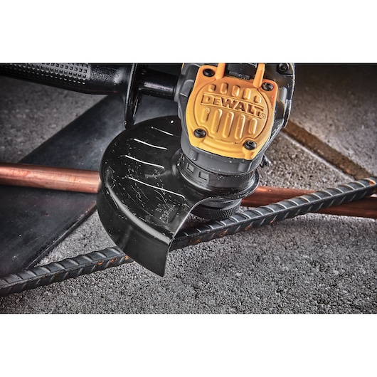 Close-up of a DEWALT angle grinder cutting through metal rods on a concrete surface.