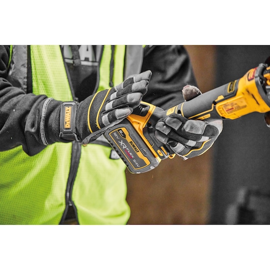 Close-up of a person wearing gloves and a high-visibility vest operating a DEWALT cordless power tool, with an XR FLEXVOLT battery attached.