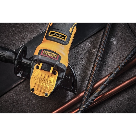 DEWALT cordless angle grinder placed on rough surface with metal rods nearby, close-up of the tool's handle.