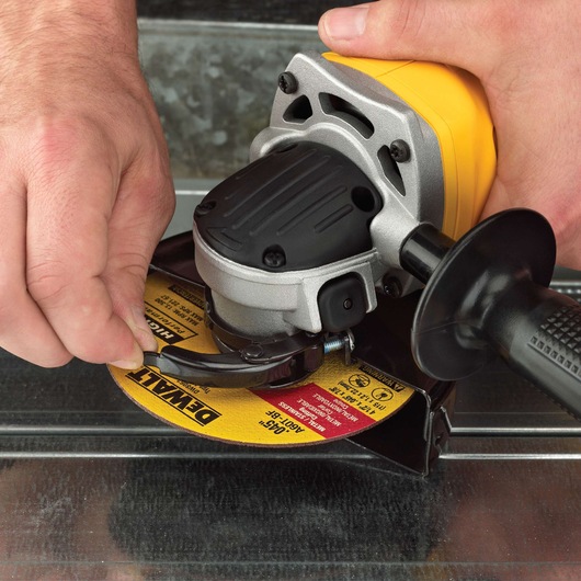 Hands adjusting a DEWALT angle grinder with a yellow grinding disc on a metal surface.
