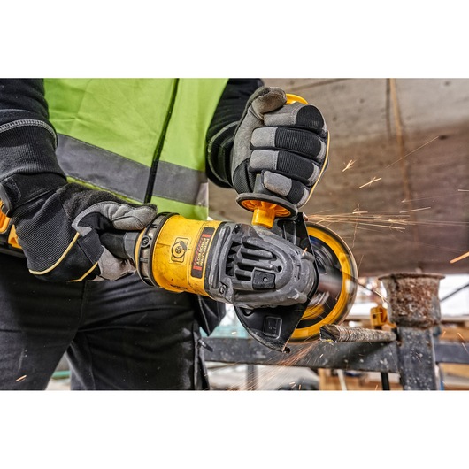 Worker uses a DEWALT angle grinder with sparks flying during metal cutting at a construction site.