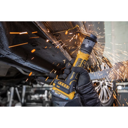 DEWALT cordless grinder creating sparks while cutting metal under a vehicle, held by a gloved hand.
