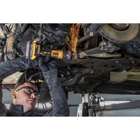 Person using DEWALT angle grinder under a car, cutting metal with sparks flying.