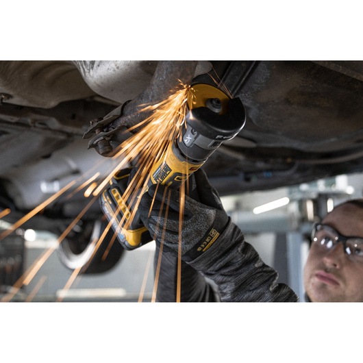 DEWALT angle grinder cutting metal under a vehicle, producing sparks. Worker wearing protective gloves.