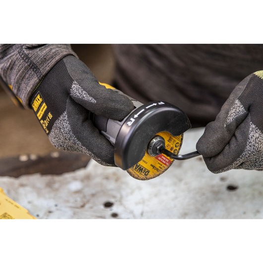 Gloved hands adjust a DEWALT grinder tool with a yellow disc on a metal surface.