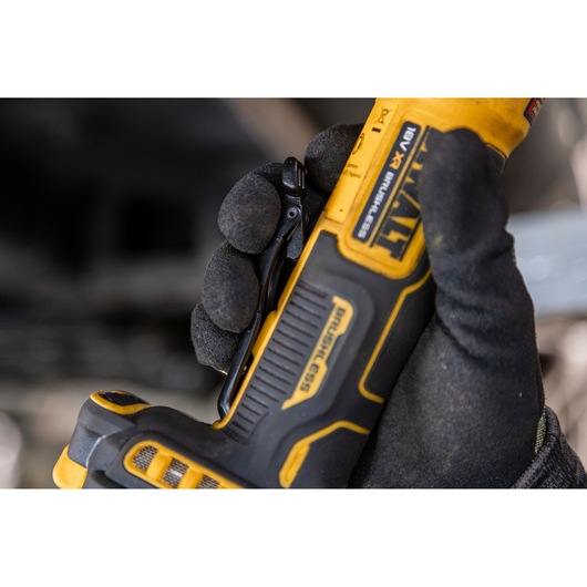 Gloved hand holding a yellow and black DEWALT 18V XR brushless tool, close-up view of handle and clip.