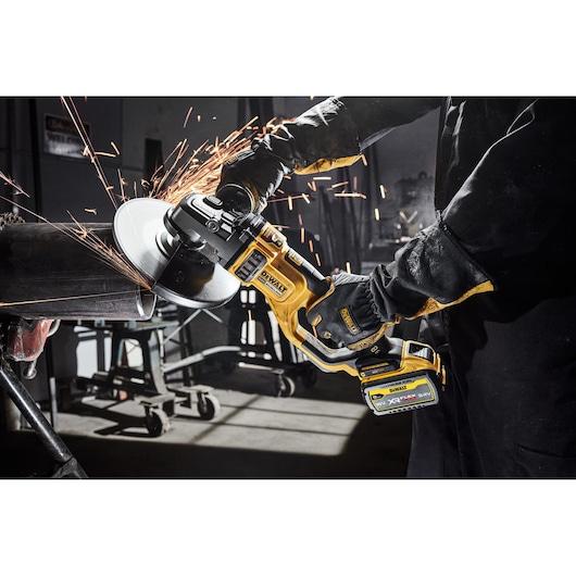 DEWALT cordless angle grinder cutting metal pipe, sparks flying in workshop setting.
