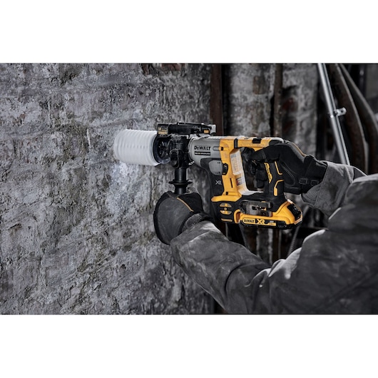 A person using a DEWALT cordless rotary hammer drill with a dust extraction attachment to drill into a concrete or brick