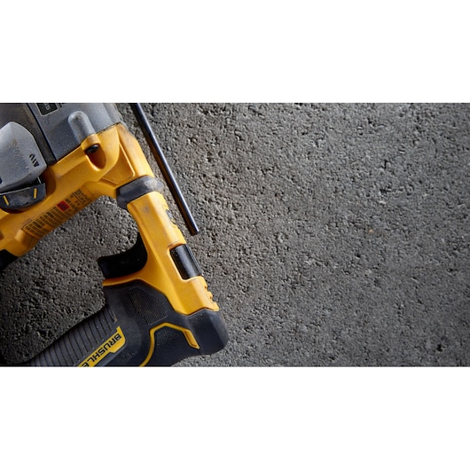 Close-up of a yellow and black DEWALT power tool with part of the handle and trigger visible, placed on a rough concrete surface.