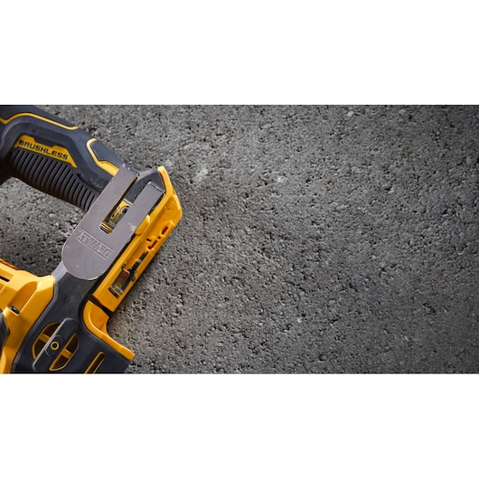 Close-up of a yellow and black DEWALT brushless power tool with part of the handle and metal attachment visible, placed on a rough concrete surface.