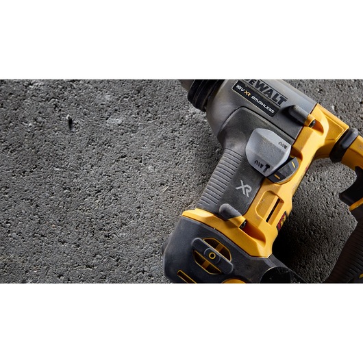Close-up view of a DEWALT 18V XR brushless power tool, partially visible, resting on a rough concrete surface.