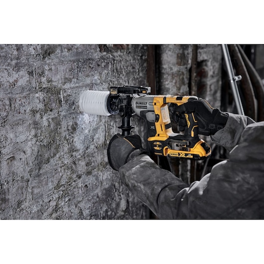 Person drills masonry wall with yellow DEWALT DCH172N rotary hammer and dust collection attachment.