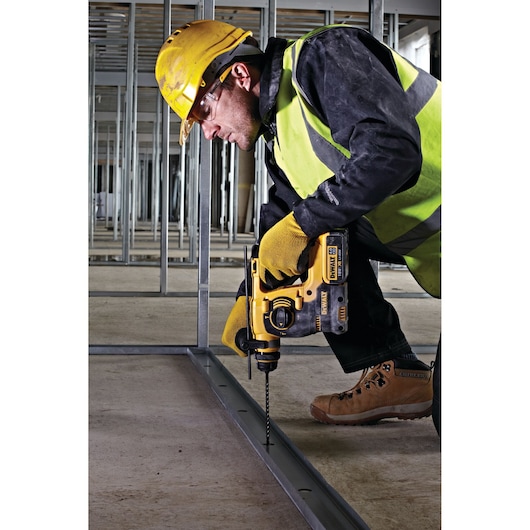 Worker drills into metal frame using a DEWALT tool, wearing safety gear at a construction site.