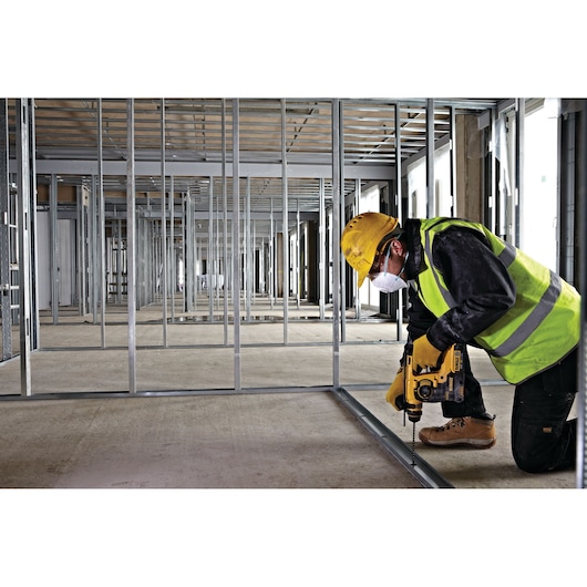 Worker uses DEWALT tool to drill metal frame, wearing safety gear in a building under construction.