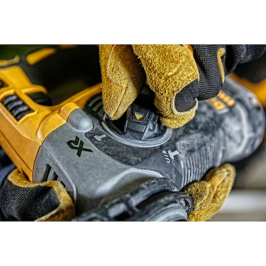 Close-up of a gloved hand adjusting the mode selector on a DEWALT power tool, showing the tool's rugged surface and control