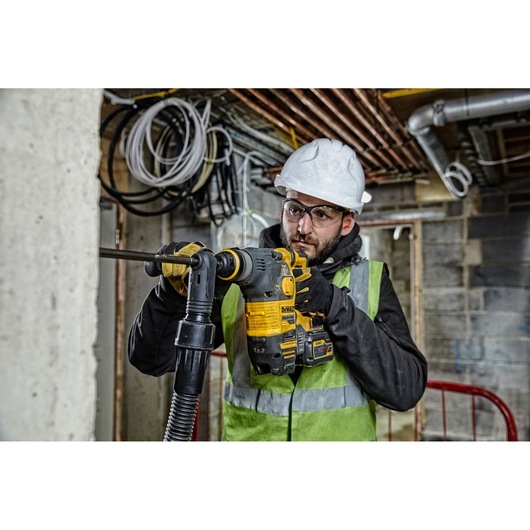 A person wearing a safety helmet and high-visibility vest is using a DEWALT DCH323T2 rotary hammer drill to work on a