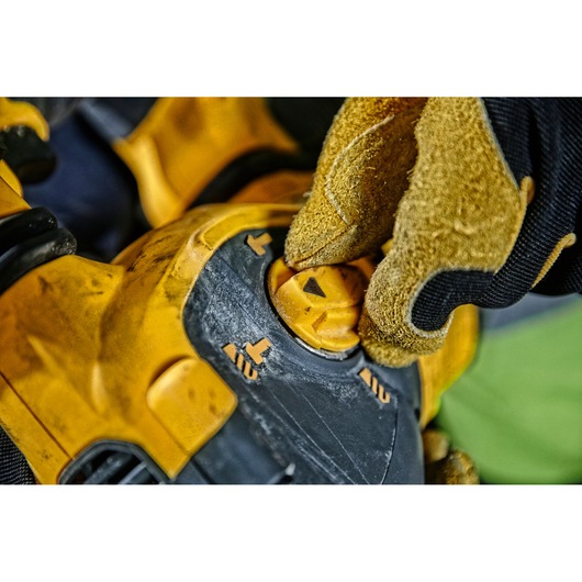Close-up of a gloved hand adjusting the settings dial on a yellow DEWALT power tool.