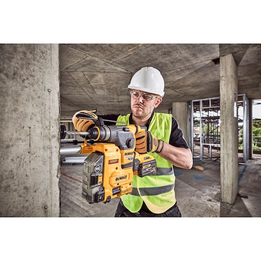 A construction worker wearing a safety helmet, gloves, and high-visibility vest is using a DEWALT DCH335X2 rotary hammer