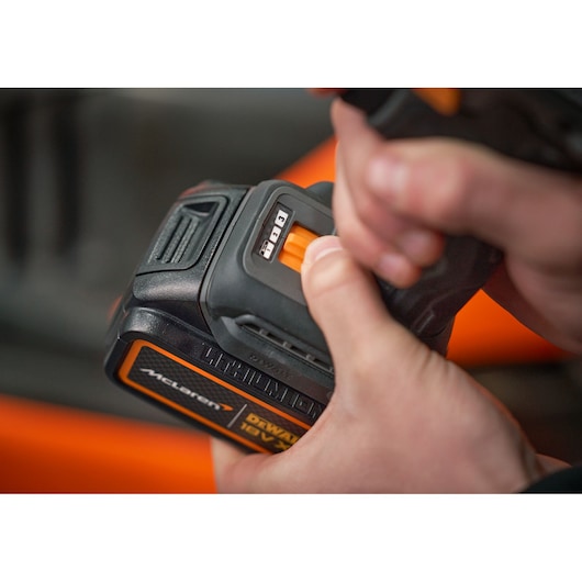 Close-up of hands holding and adjusting a DEWALT lithium battery with an orange slider and indicator lights.