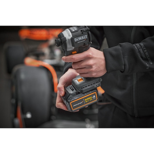 Hand holding a DEWALT 18V power tool with McLaren branding, car blurred in the background.