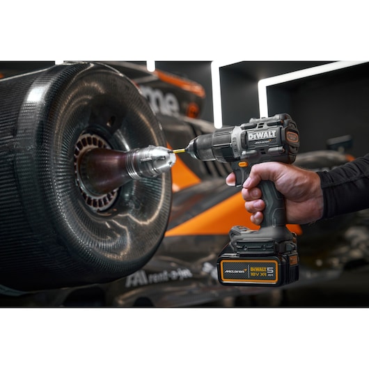 A DEWALT cordless drill being used to work on the wheel area of a racing car, with the drill prominently showing its branding and specifications.